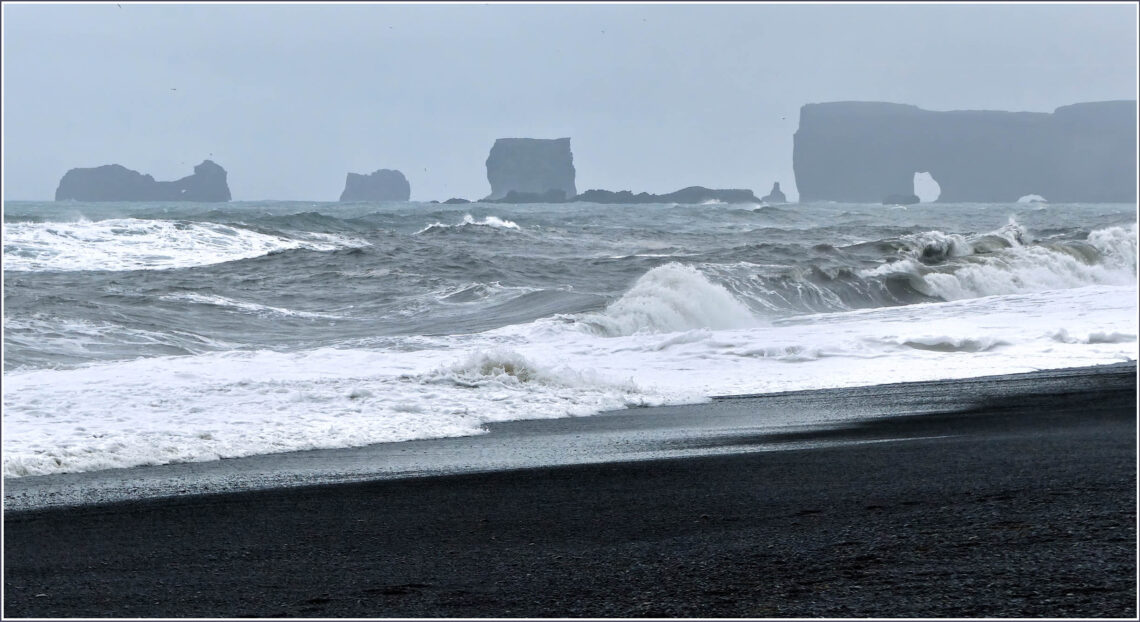Black beach with distant cliffs with a rock arch