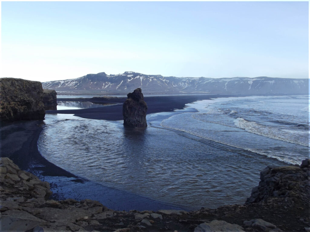 Looking down at a black beach with rock stacks and distant mountains