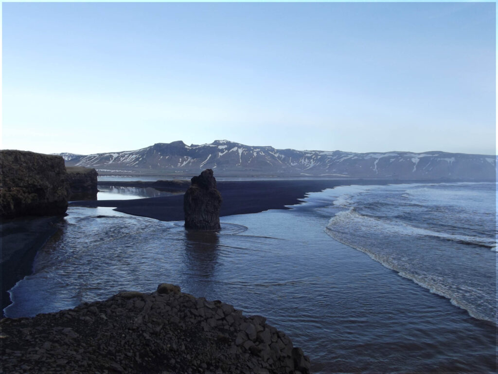 Looking down at a black beach with rock stacks and distant mountains