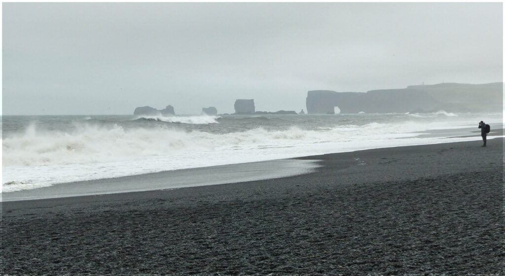 Beach with a man taking photos and distant cliffs with an arch